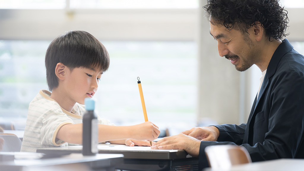市民参加型ワークショップで、専門家の助言を受けながら学習に取り組む小学生の男の子と指導する男性の様子のイメージ画像