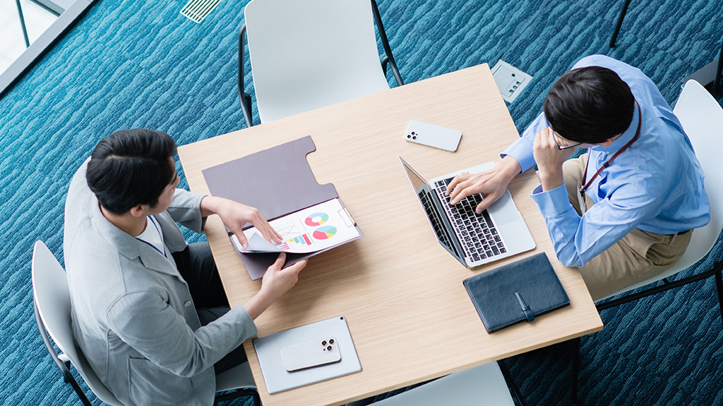 真上のアングルで二人が対面で打合せをしているイメージ画像